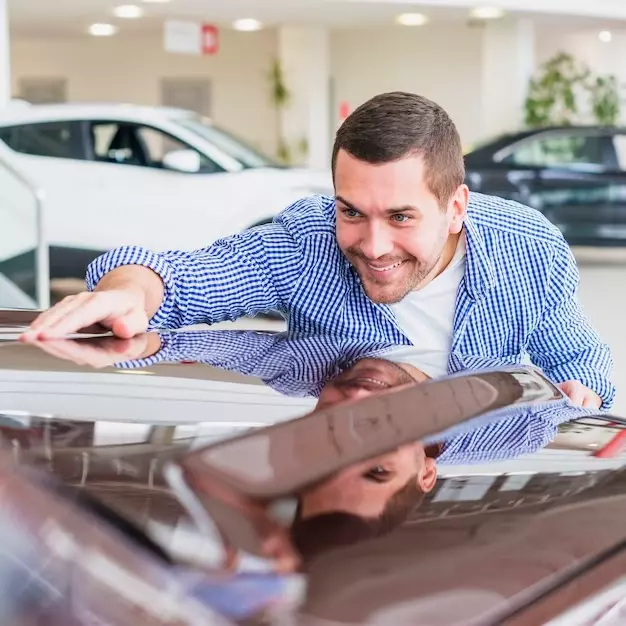 um rapaz feliz, sorrindo agachado, apalpando a frente do carro, analisando o carro